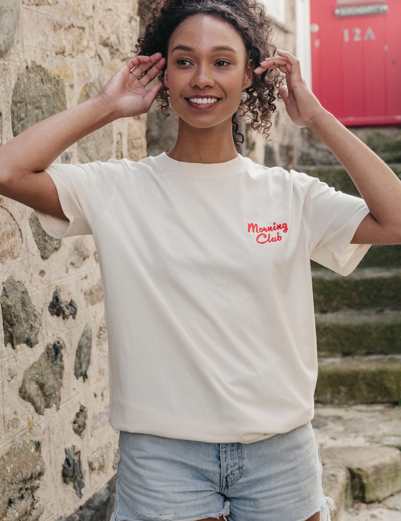 A lady wearing a natural printed graphic t-shirt, with a illustration of a breakfast fry up, set in a town.