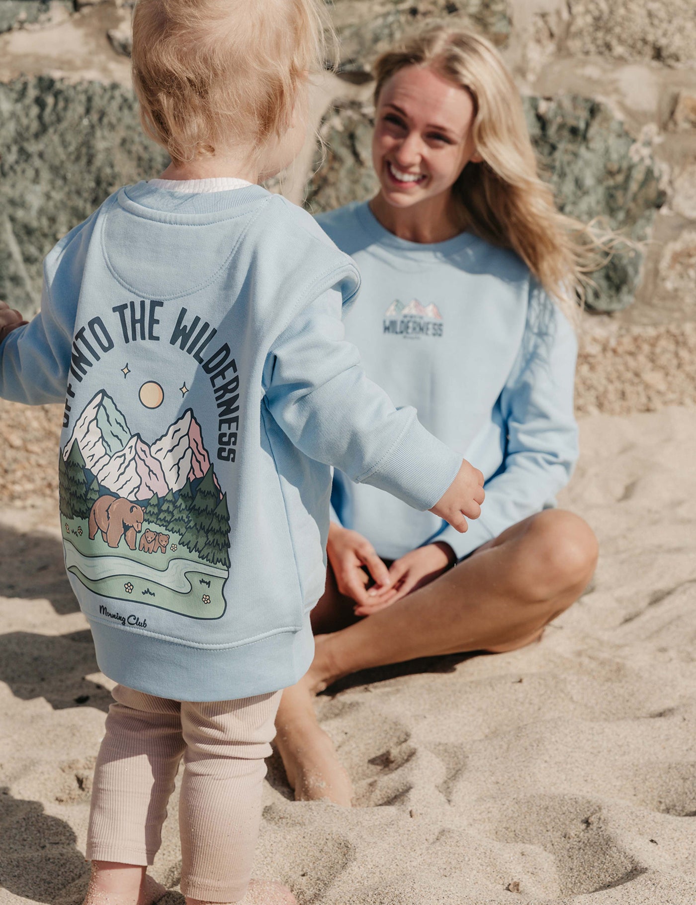 Lady wearing a printed sweatshirt, that says into the wilderness, and its set on the beach.