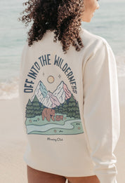Lady wearing a printed sweatshirt, that says into the wilderness, and its set on the beach.