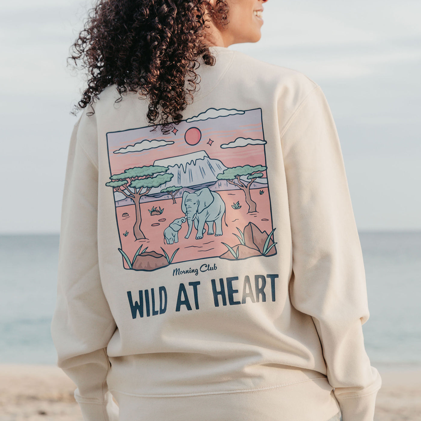 Lady wearing a printed sweatshirt, that says wild at heart, and its set on the beach.