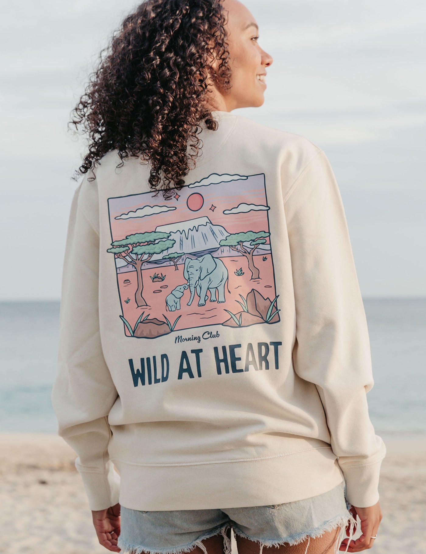 Lady wearing a printed sweatshirt, that says wild at heart, and its set on the beach.